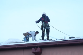Two men work of repairing the roof of the gym which has been leaking to the point of disrupting 2 girls basketball games and even Homecoming Coronation.
