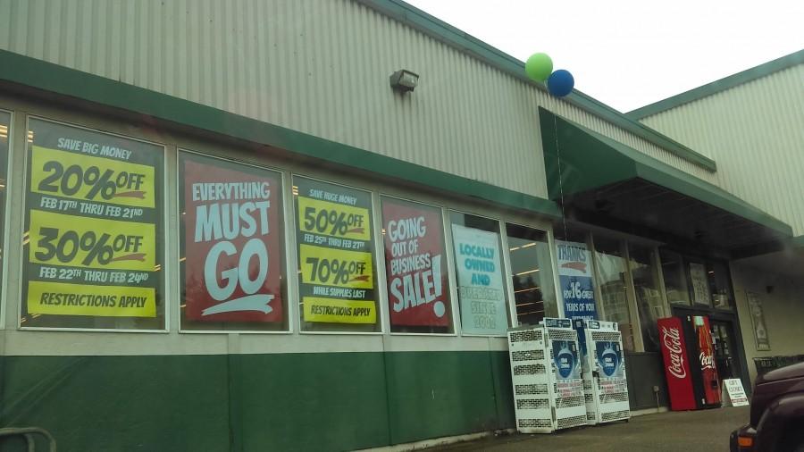 SIgns hang in the window of Rogers Market, reading EVERYTHING MUST GO and sales being held on the leftover items.