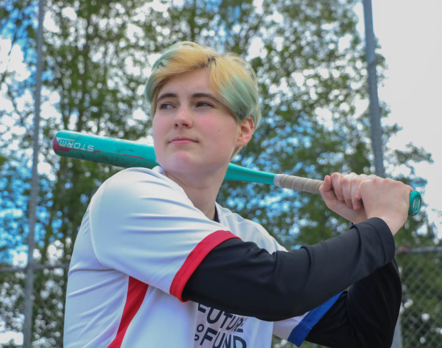 Emma Kerani, still holding a softball bat over their shoulder, looking heroically off into the distance like theyre a superhero ready to save the day.