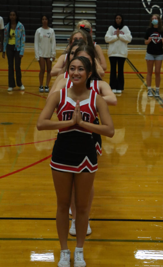 Senior cheerleader Alaya Bulatao-Quang standing with her hands clasped together and a smile on her face, in position to start the dance Supersonic to a crowd of new freshmen. Behind her is a line of other cheerleaders and a group of Connect leader seniors, all in the same pose.