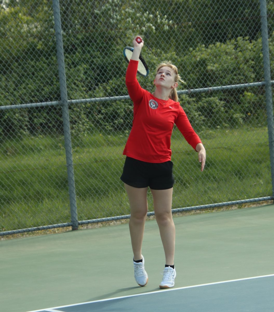 Senior Angela Grachev keeping an eye on the ball as she goes to serve during a tennis match.
