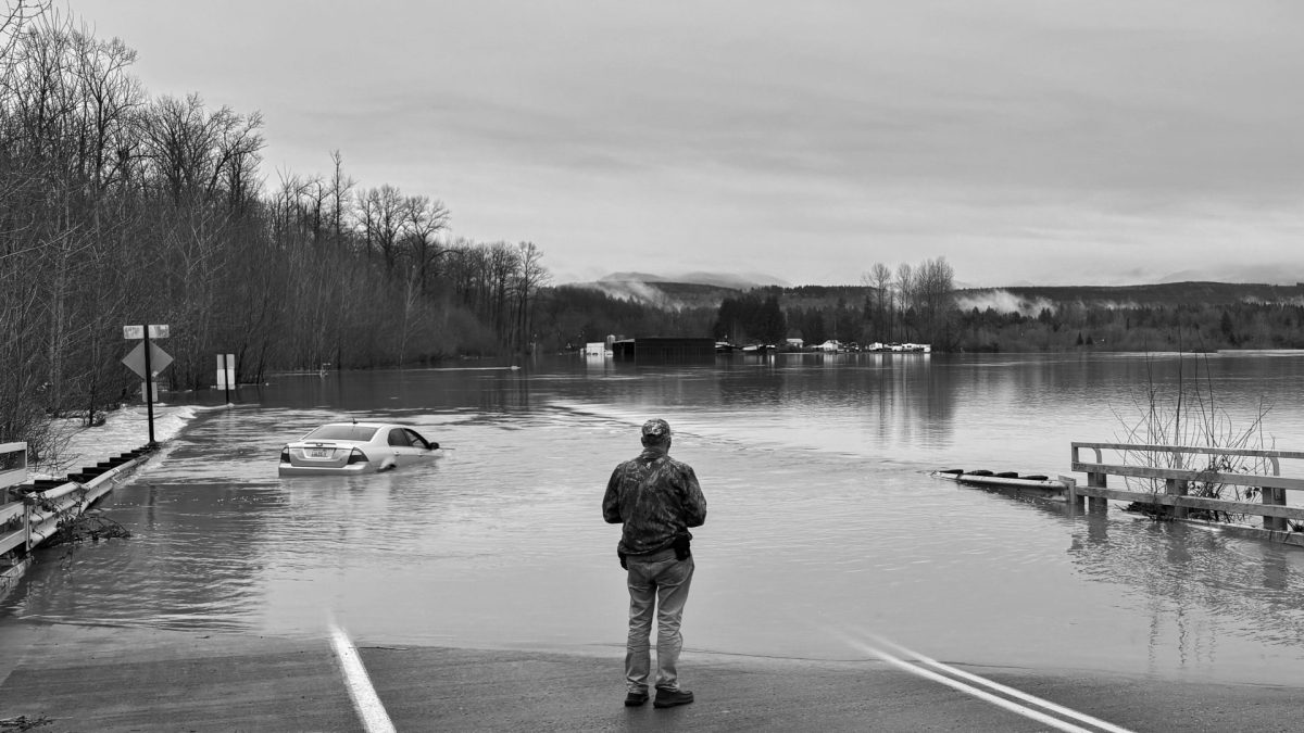 A resident of Issaquah stands looking out at the flooded road, an abandoned car. Image courtesy Owen Kelly